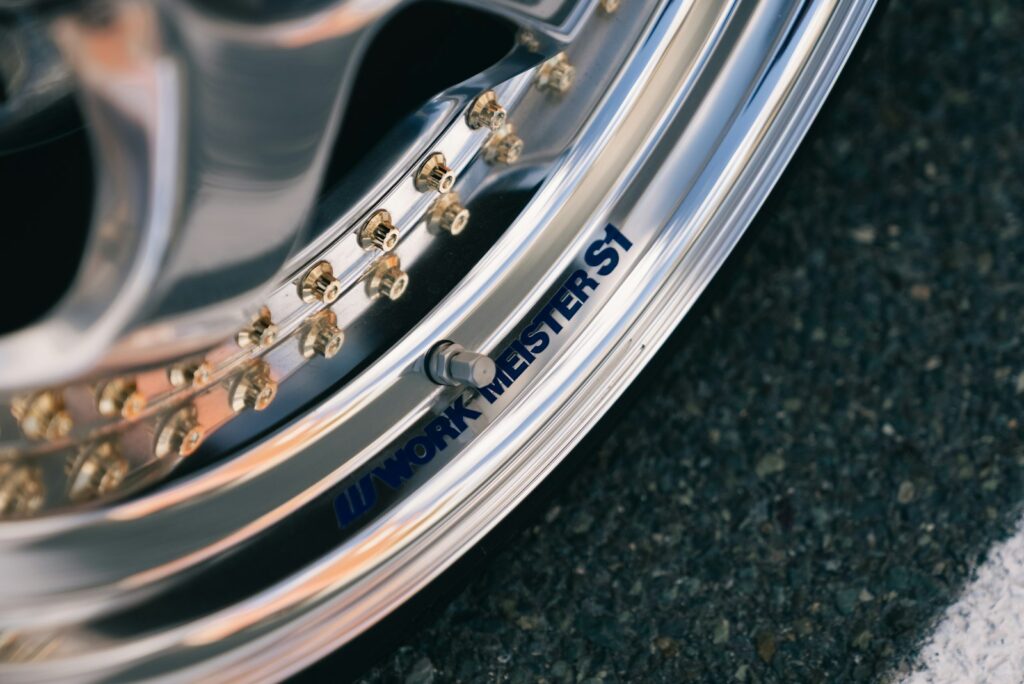 Polished chrome car wheel with gold bolts on asphalt, an example of decorative metal finishing