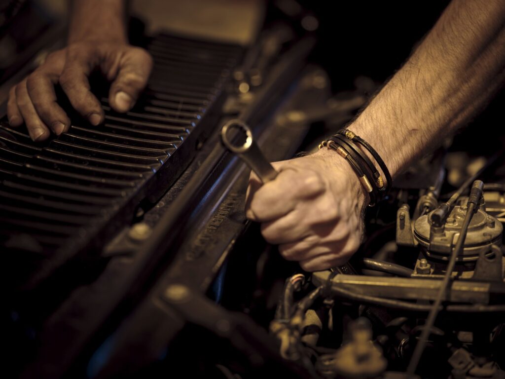 Greasy hands using a metal wrench on a car engine, representing repair rather than replacement
