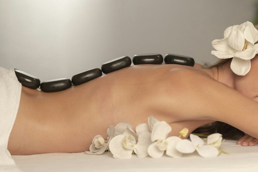 Person lying on a massage table with smooth black stones placed on their back
