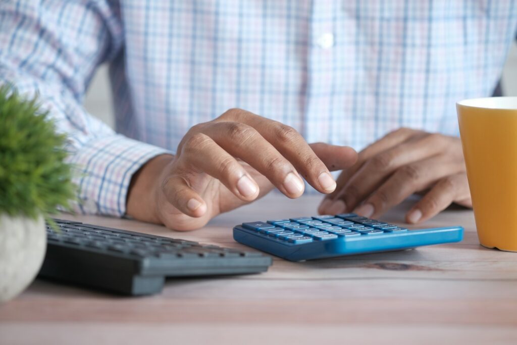 Close-up of a hand using a calculator at a desk beside a coffee mug, working through figures