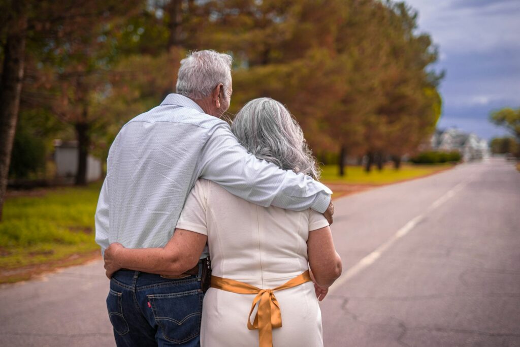 Older man and woman with grey hair walking arm in arm down a road