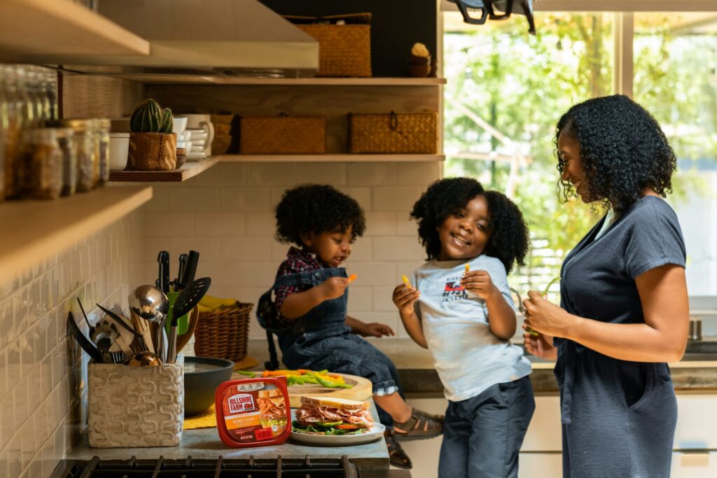 Woman and two children preparing sandwiches in a sunlit kitchen, a welcoming family home setting