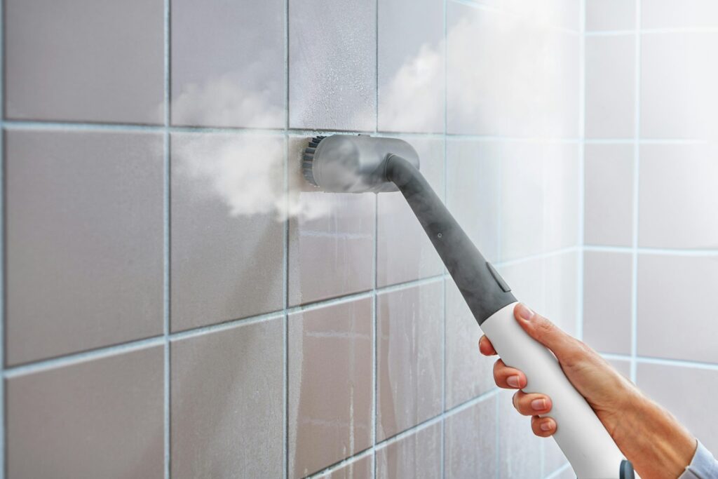 Steam cleaner sanitising a tiled bathroom wall, part of regular bathroom cleaning and upkeep